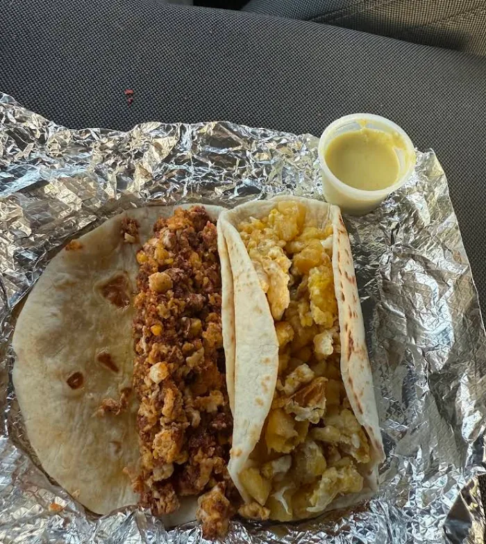 Two breakfast tacos on flour tortillas, one chorizo and egg and one potato and egg, with a side of salsa.