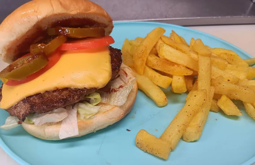 A classic Hamburguesas Emilia cheeseburger with melted American cheese, fresh tomato, jalapeños, and lettuce on a soft bun, with a pile of golden seasoned fries.