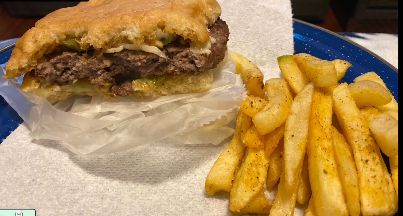 A thick cheeseburger cut in half on a blue enamel plate, showing the juicy beef patty and melted cheese, with a pile of golden seasoned fries.