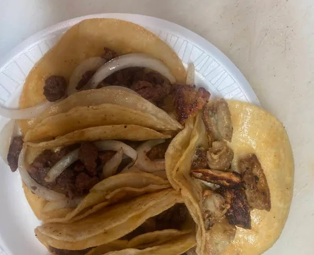 Street tacos on double corn tortillas topped with grilled meat and raw onion.